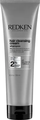 A close-up studio shot of a Redken hair cleansing cream shampoo bottle against a light gray background.