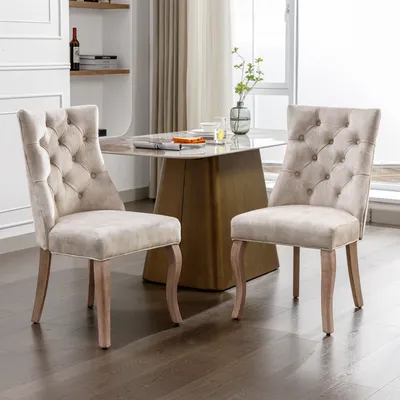 Two beige dining chairs are placed in a dining room setting, with a dining table and shelves in the background.