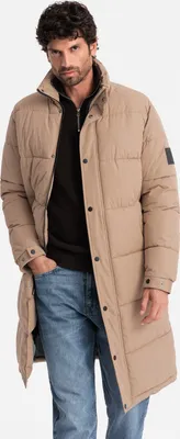 A man wearing a beige winter jacket and blue jeans.