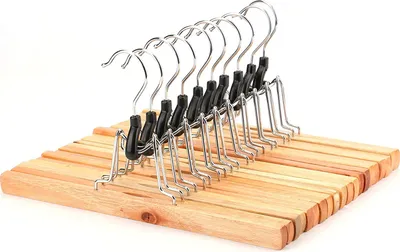 A row of wooden hangers with metal clips for hanging pants or skirts, set against a white background.