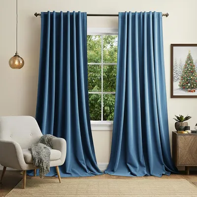 A living room scene with blue velvet curtains framing a window, a chair with a blanket, and a side table with a Christmas-themed picture.