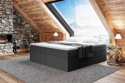 A bedroom with a large window overlooking a snowy mountain landscape. The bed is the central focus, with a fireplace and stone wall on the left.