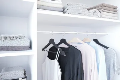 A clean, organized closet with clothes hanging on a rod and folded items on shelves.