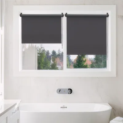 A bathroom with a bathtub and a window covered by roller blinds.