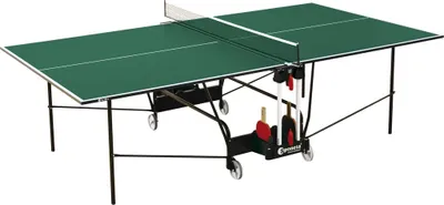 A green ping pong table with a net, set up on a white background. It has a black frame and wheels, and a storage rack underneath holding paddles and balls.