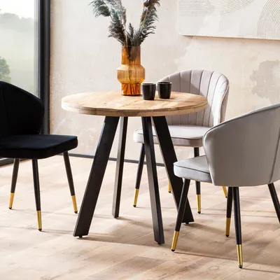 A round wooden dining table with black legs and gold accents, surrounded by three chairs (one black, two light gray).