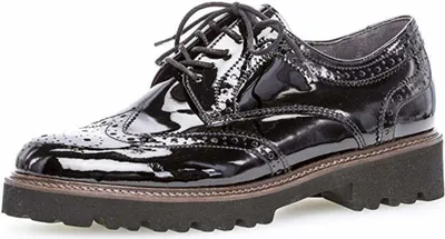 A black patent leather wingtip shoe with a thick sole.