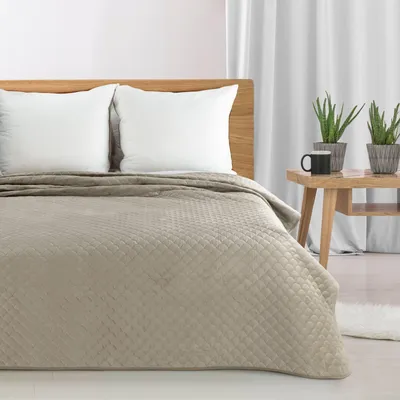 A beige quilted bedspread is laid out on a bed with two white pillows.