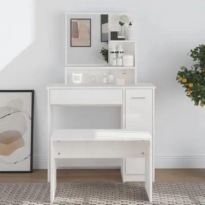 A white vanity table with a mirror and stool, set against a white wall with a framed picture on the left and a plant on the right.