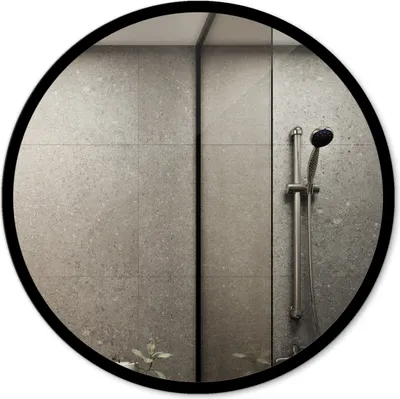 A round mirror with a black frame reflecting a modern bathroom with gray tiled walls and a shower head.