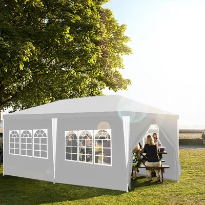 People are sitting at a picnic table under a gray tent in a park setting.