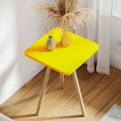 A yellow side table with wooden legs, decorated with a vase of dried flowers and a diffuser.