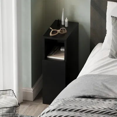 A black bedside table next to a bed, with a curtain and a basket in the foreground.