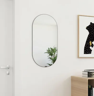 A mirror is mounted on a white wall next to a door and a framed picture.