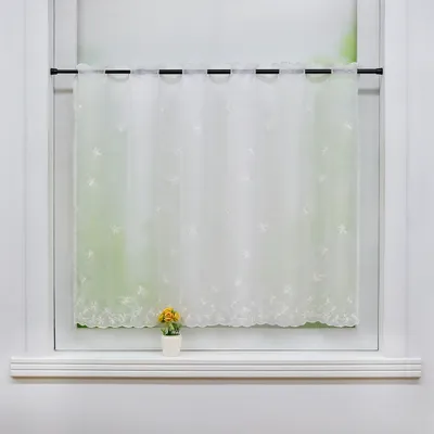 A white lace curtain with embroidered flowers hangs on a window rod, with a small potted yellow flower on the windowsill below.