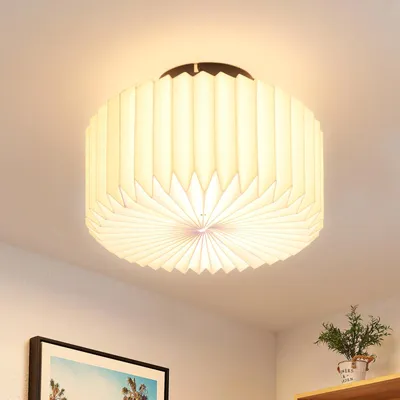 A ceiling lamp with a pleated paper shade is mounted on a white ceiling.