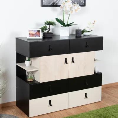 A modern dresser with a black and cream finish, decorated with plants and a framed picture.