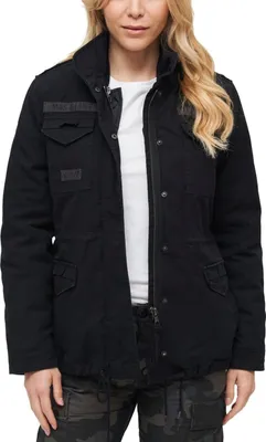 A woman wearing a black jacket and camouflage pants, posing against a white background.