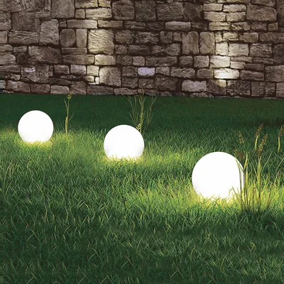 Three illuminated spherical garden lights are placed on a grassy lawn in front of a stone wall.