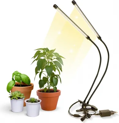 A product shot of a dual-headed LED plant grow light with three potted plants.