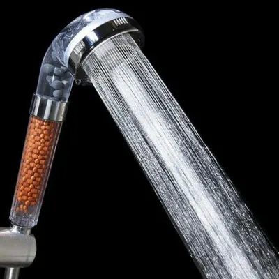 A close-up shot of a shower head with water spraying out, against a black background.