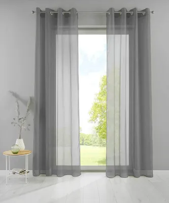 A pair of sheer grey curtains hanging in front of a window with a view of trees and sky.