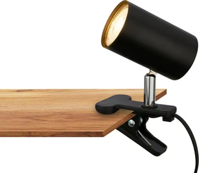 A black desk lamp with a gold interior is clamped to a wooden surface.