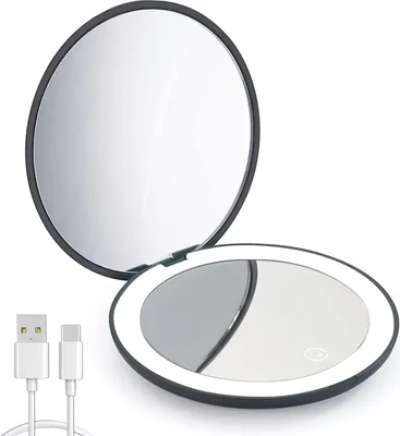 A black, round, foldable makeup mirror with a white LED light ring around the edge of the open mirror. A white USB-C charging cable is shown in the foreground.