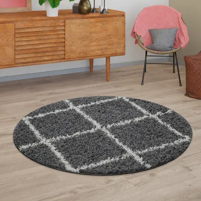 A round gray rug with a white diamond pattern is placed on a wooden floor in a room with a wooden cabinet and a chair.