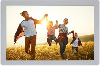 A family is running through a field of tall grass at sunset, holding hands and smiling.