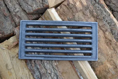 A cast iron grate lies on a pile of firewood.