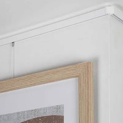 A close-up view of a picture hanging system installed on a wall and ceiling corner, with a framed artwork partially visible.