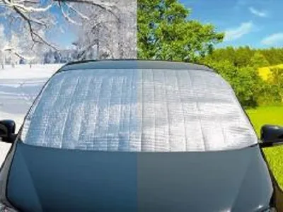 A car windshield covered with a reflective sunshade, split between a winter scene and a summer scene.