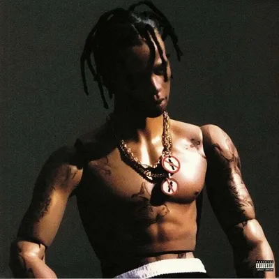 A close-up shot of a male mannequin with dreadlocks, wearing a gold chain with two circular pendants, against a dark gray background.
