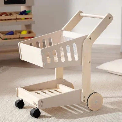 A wooden toy shopping cart is shown on a rug in a room.