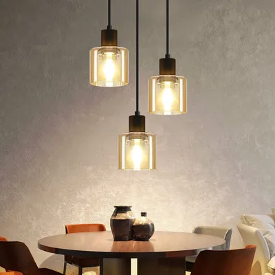 A dining table with three pendant lights hanging above it, and two decorative vases on the table.