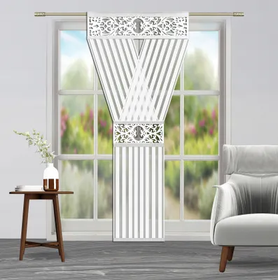 A decorative curtain panel hanging in a window with a small table and vase to the left and an armchair to the right.