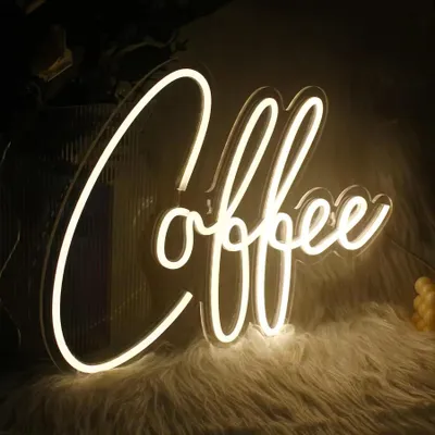 A white neon LED sign shaped like the word "Coffee" is displayed on a furry white surface, with a dark background.