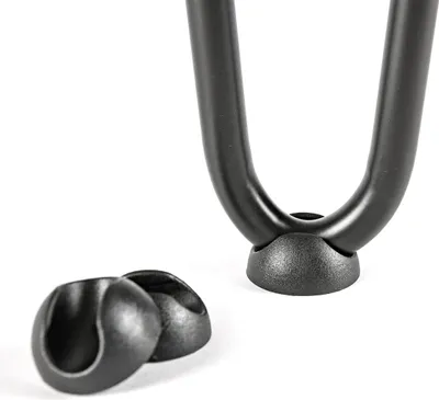 A close-up view of black floor protectors for hairpin legs, with two protectors in the foreground and one attached to a hairpin leg in the background.