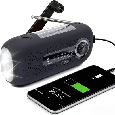 A black emergency radio with a flashlight and antenna is shown next to a smartphone that is charging.