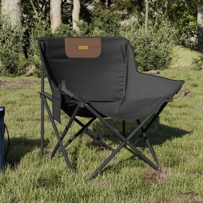 A black camping chair with a brown accent is set up on a grassy area with trees in the background.