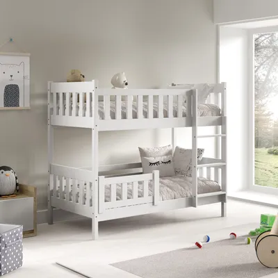 A white wooden bunk bed with bedding and pillows in a child's room, with a window in the background.