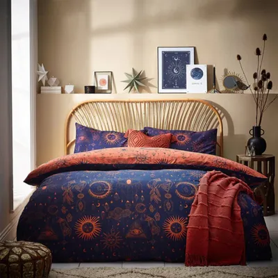 A bedroom scene with a bed dressed in celestial-themed bedding, a rattan headboard, and decorative items on a shelf.