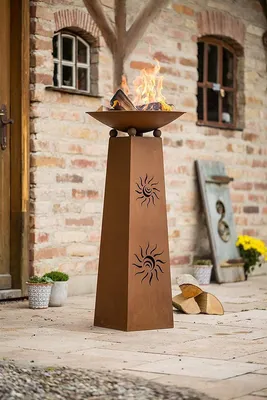 A metal fire pit with a sun design on a stone patio.