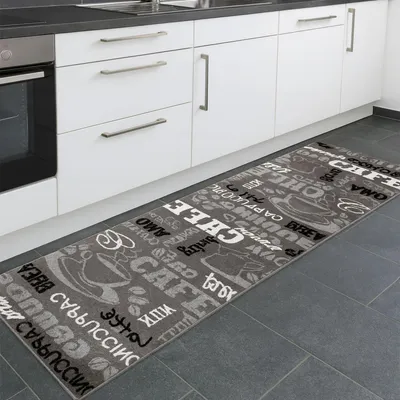 A kitchen runner rug with a coffee-themed pattern is placed in front of white kitchen cabinets.