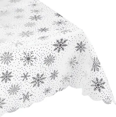 A close-up, angled view of a white tablecloth with a silver snowflake pattern.
