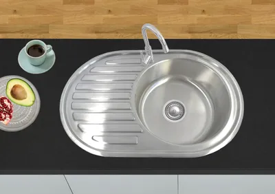 A stainless steel kitchen sink with a faucet, a cup of coffee, and a plate with avocado and pomegranate seeds on a black countertop.