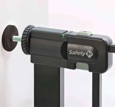 A close-up view of a black metal safety gate mechanism, showing the mounting hardware and the 'Safety 1st' logo.