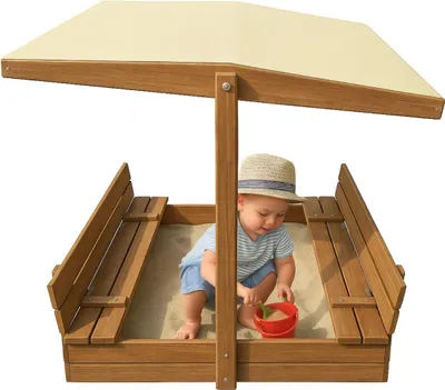 A baby playing in a wooden sandbox with a canopy.