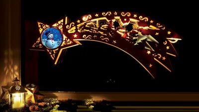 A festive Christmas decoration shaped like a shooting star, illuminated by warm white LEDs, displayed in a window at night.